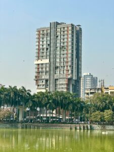 A tall residential building overlooking a lake with palm trees in Mumbai, India.